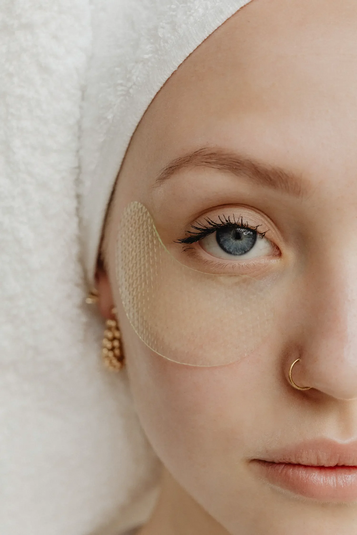 Halbes Frauengesicht mit Augenpatches, Nasenring und Handtuch auf dem Kopf