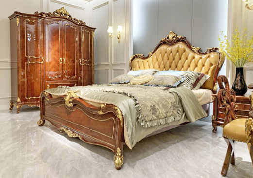 Luxurious bedroom with a large wooden bed featuring gold embellishments and tufted golden headboard, a matching wardrobe, and a vase with yellow flowers on a side table.