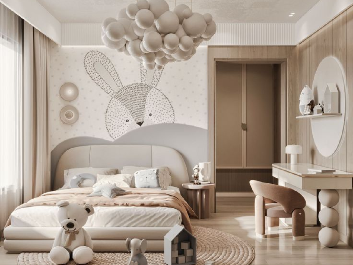 A child's bedroom with a large bunny illustration on the wall, a cloud-shaped light fixture overhead, a bed with plush pillows and toys, a teddy bear on the floor, and a writing desk with a chair.
