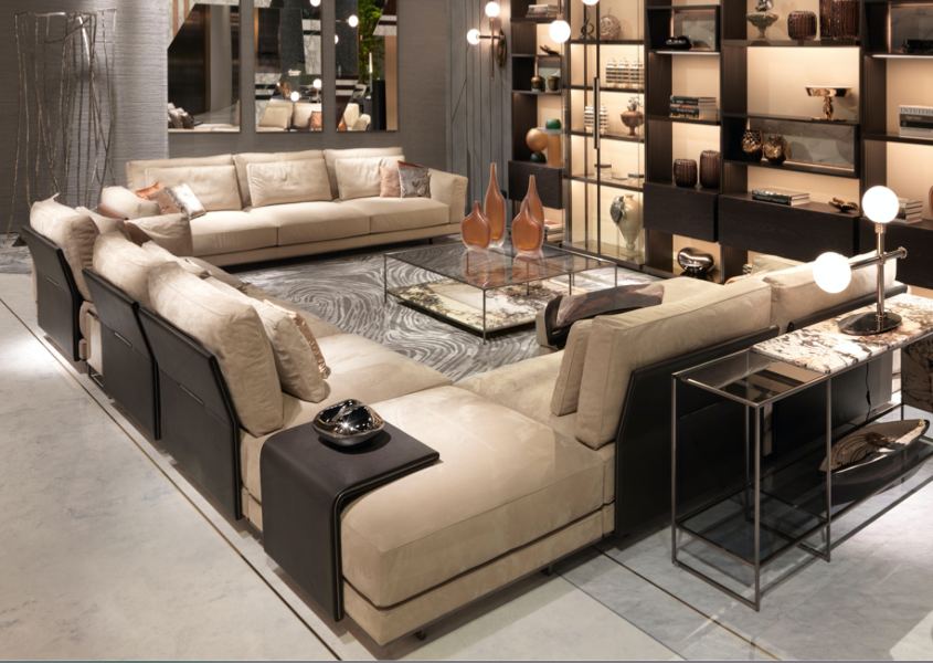 Modern living room with beige sectional sofa, glass coffee table, decorative vases, black metal side tables with lamps, and built-in shelving with decorative objects.