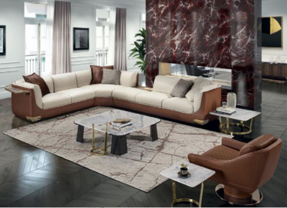 Modern living room with a large L-shaped beige sectional sofa, a marble-top coffee table, a brown armchair, and a patterned area rug. There is a tall marble accent wall, floor-to-ceiling windows with curtains, and decorative pillows on the sofa.
