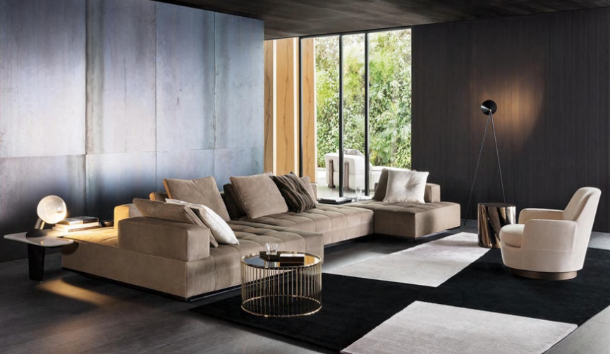 Modern living room with a beige sectional sofa, white armchair, black and white area rugs, minimalist side tables, and large window with green trees outside.