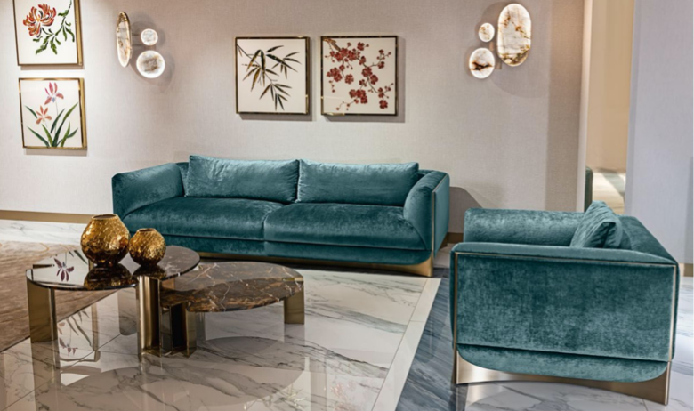 Living room with a turquoise velvet sofa, matching armchair, marble coffee table with brass accents, decorative gold vases, and framed botanical art on the wall.