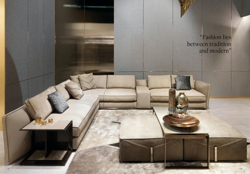 Elegant living room with beige sectional sofa, gray accent pillows, a side table with drinks, a large plush rug, and decorative vases on the coffee table. Wall has quote 'Fashion lies between tradition and modern.'