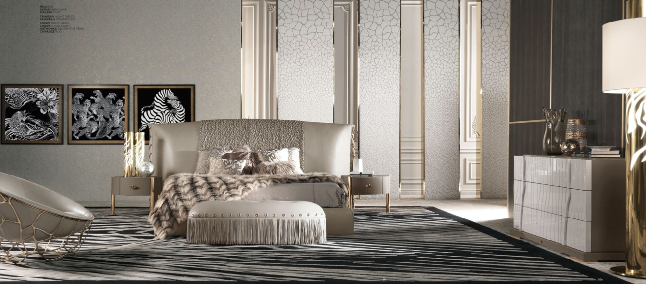 Modern bedroom with beige upholstered bed, fur throw, abstract black and white artwork, black and white zebra striped rug, white side tables, and decorative vases.