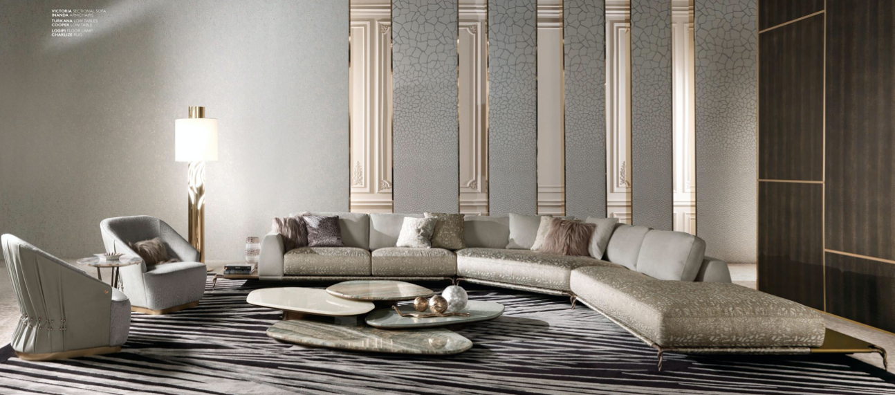 Modern living room with curved sectional sofa, two armchairs, a sculptural floor lamp, and layered coffee tables on a zebra print rug, with metallic and textured wall panels.