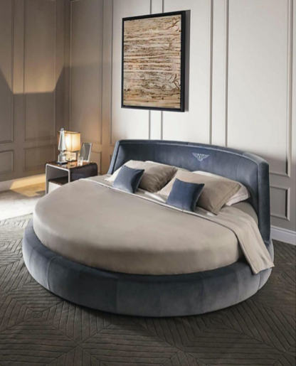 Modern bedroom featuring a round bed with a velvet headboard, decorative pillows, a side nightstand with a lamp, and abstract artwork on the wall.