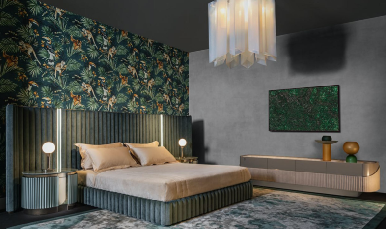Modern bedroom with a green velvet bed, tropical wallpaper, nightstands with lamps, a wall-mounted TV, and decorative vases, with a pendant ceiling light.