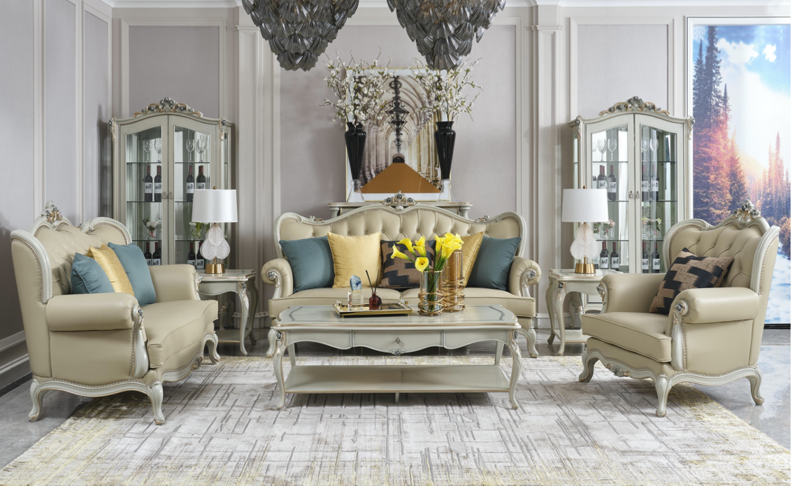 Elegant living room with cream-colored vintage-style sofa and armchairs, glass display cabinets, a coffee table with flowers, and a large window showing a scenic mountain landscape.