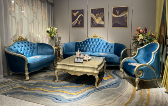 Elegant living room with blue velvet tufted sofas, a cream coffee table, floral arrangements, and framed abstract art on the wall.