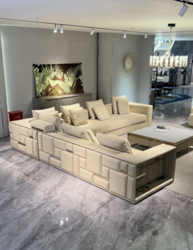Living room with beige sectional sofa and pillows, coffee table, wall art, and a kitchen area in the background.
