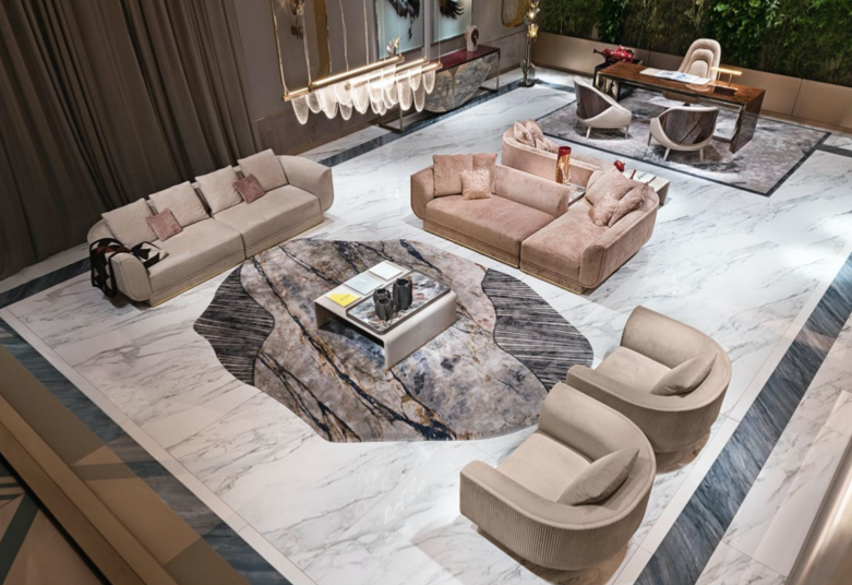 A spacious, modern living room with white marble floors, featuring multiple sofas and armchairs, a central marble coffee table on an abstract patterned rug, and a separate workspace or dining area with a wooden table and chairs, decorated with contem