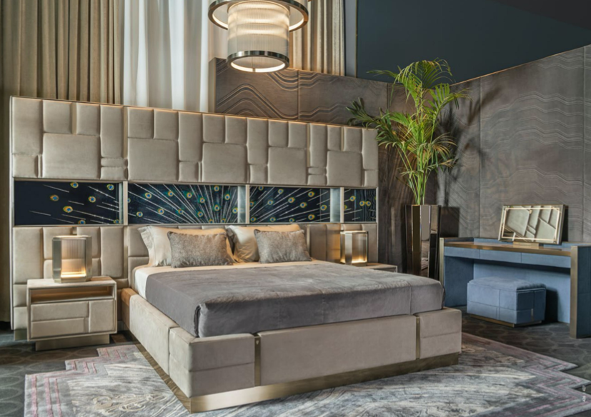 Modern bedroom with large upholstered bed, nightstands with lamps, tall plant, vanity with mirror and stool, and decorative wall art in a high-end hotel or apartment.