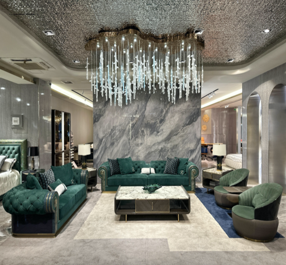 Luxurious hotel lobby with green velvet sofas, marble coffee table, and modern chandelier. The area features gray marble walls and archways with additional seating in the background.