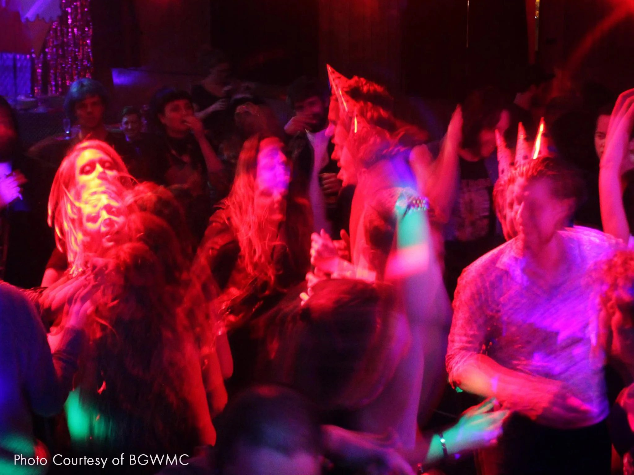 People dancing at a party with colorful lights and some wearing party hats.