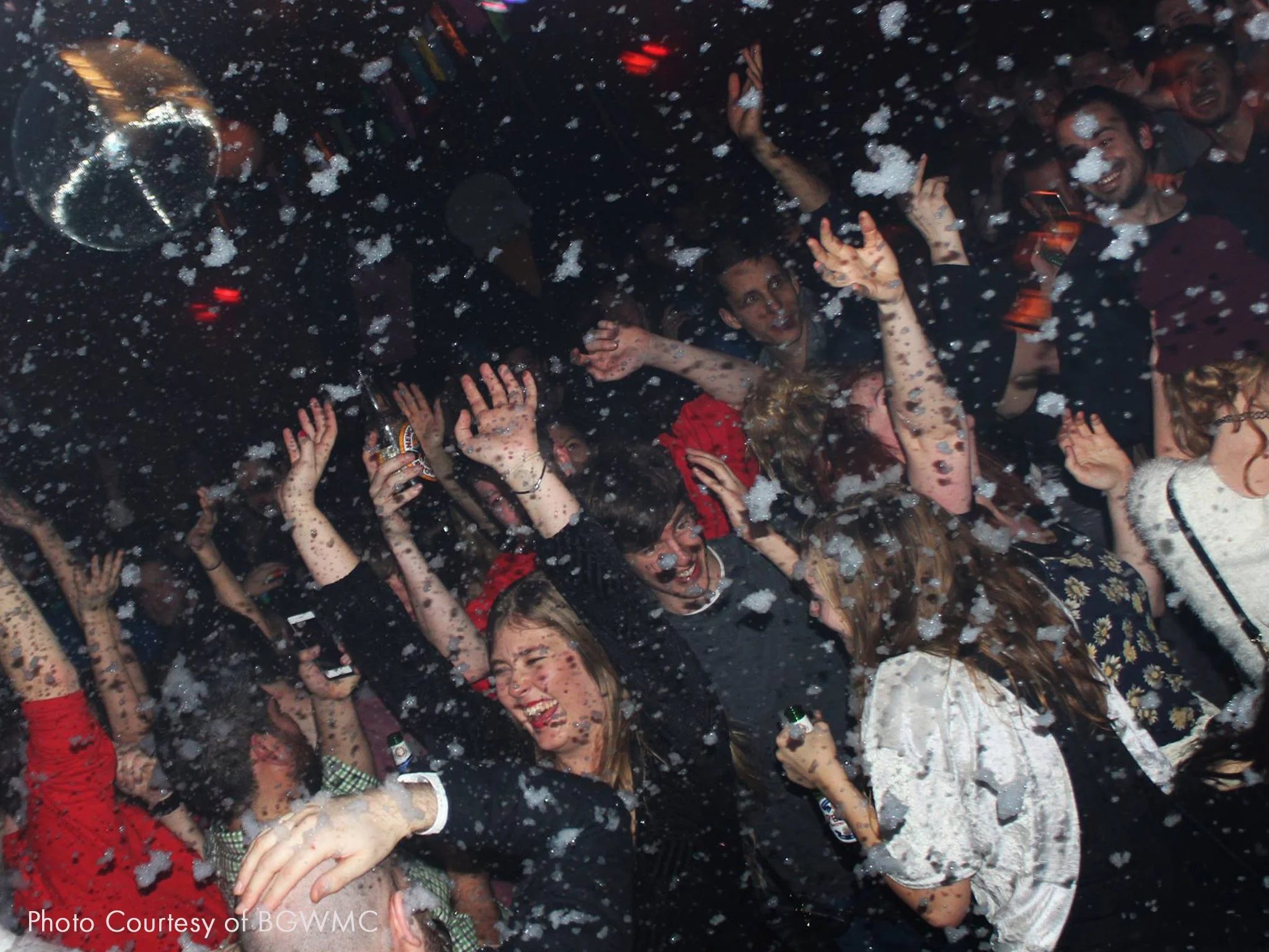 People dancing and celebrating in a nightclub with foam falling from above.