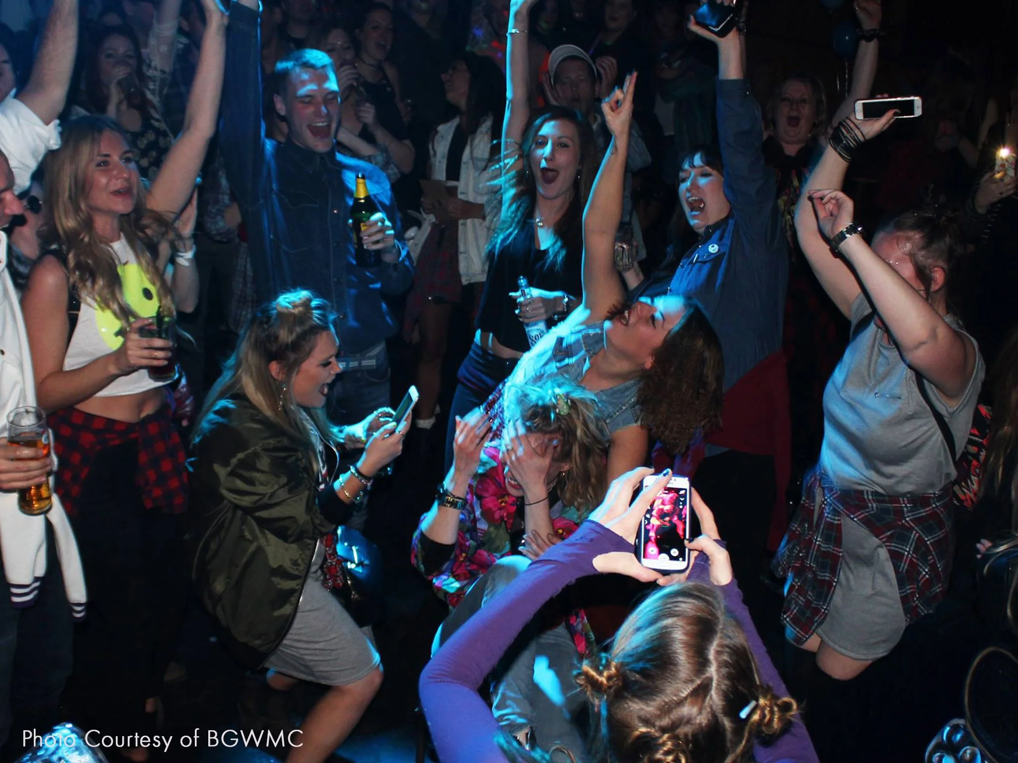 Group of people dancing and celebrating at a party. They are watching someone dance and are cheering them on.
