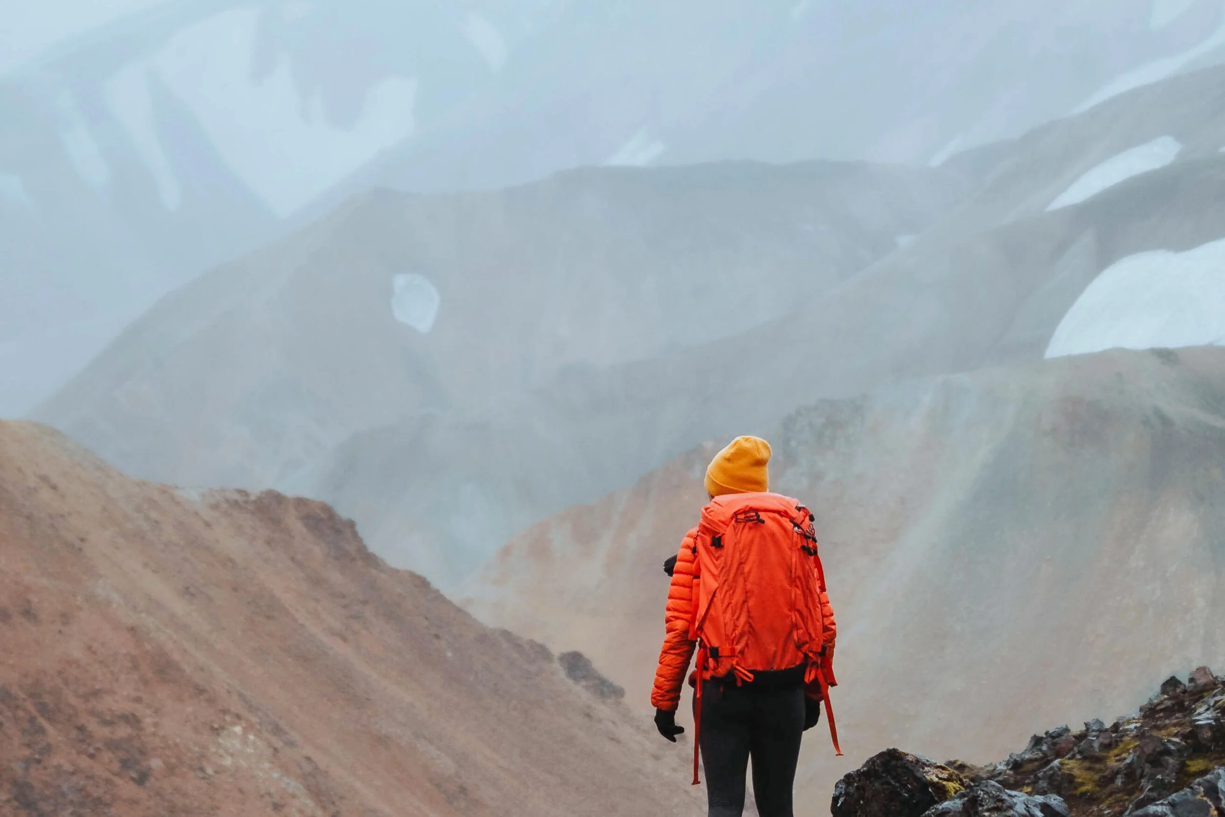 Woman with orange jacket and backpack standing at a mountain overlook, representing the journey of personal growth, self-discovery, and ADHD coaching.