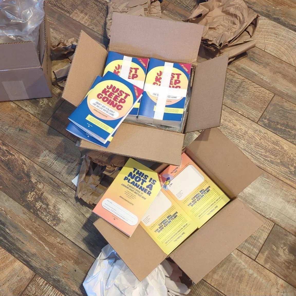 Open shipping boxes containing Just Keep Going ADHD goal-setting workbooks and planners designed to help adults navigate change and achieve meaningful goals.