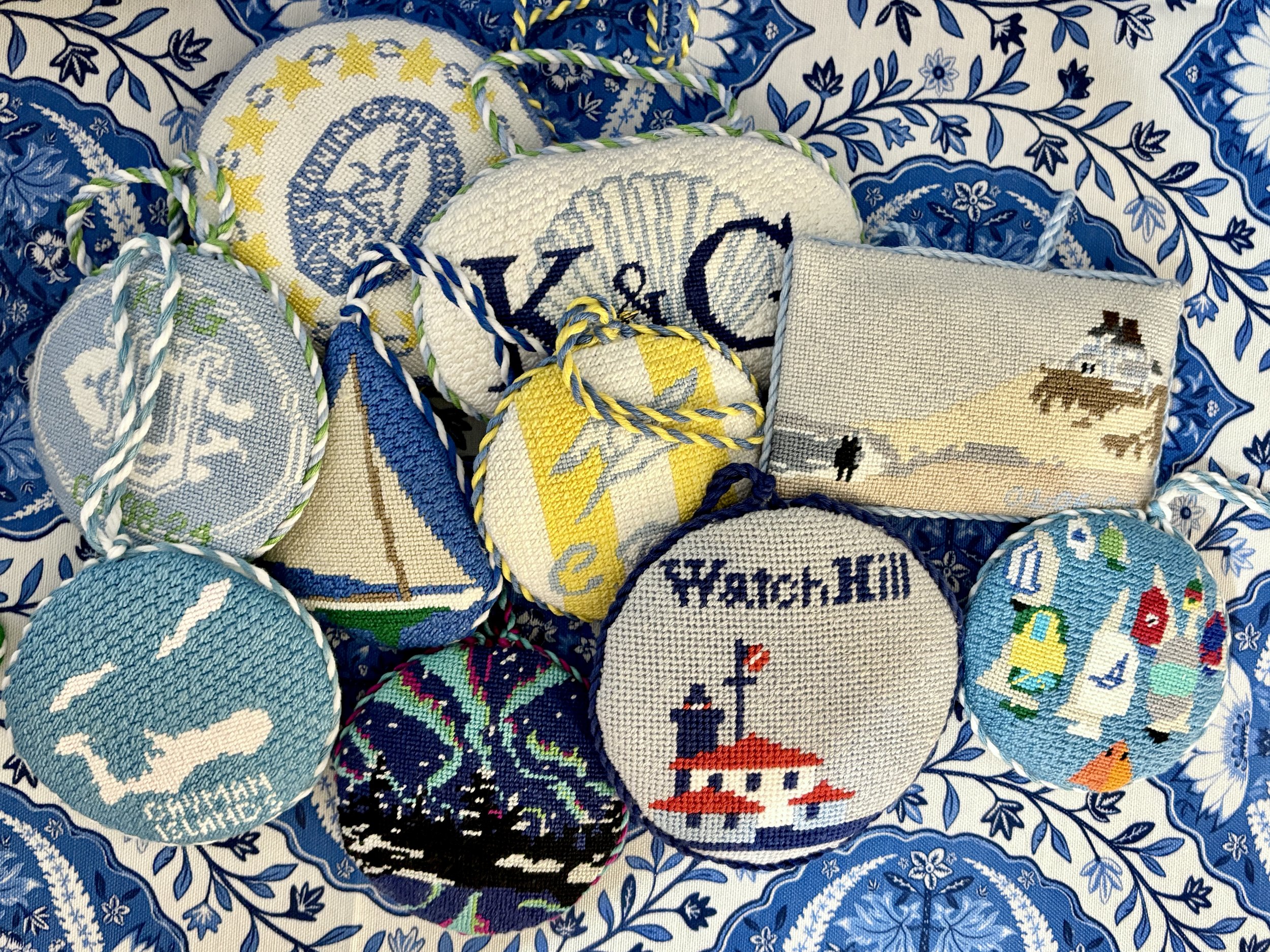 Cross-stitched ornaments featuring nautical, beach, and winter themes, arranged on a blue patterned fabric background.