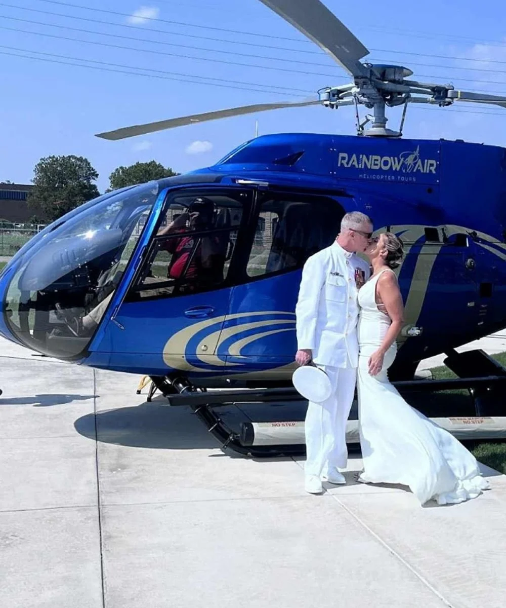 New couple stands in front of a helicopter kissing in their wedding clothes