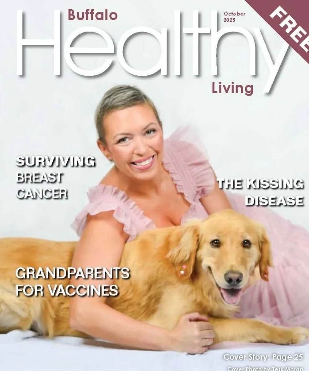 A woman with short hair wearing a pink ruffled dress is laying on a white surface next to a golden retriever dog. The woman is smiling and the dog is relaxed with its tongue slightly out.