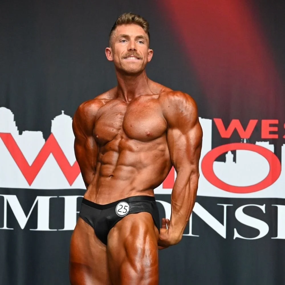 Male body builder poses on stage with a dark, competition tan by Pure Luxe