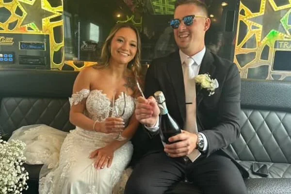 Bride with a natural spray tan pops champagne in a limo with her groom