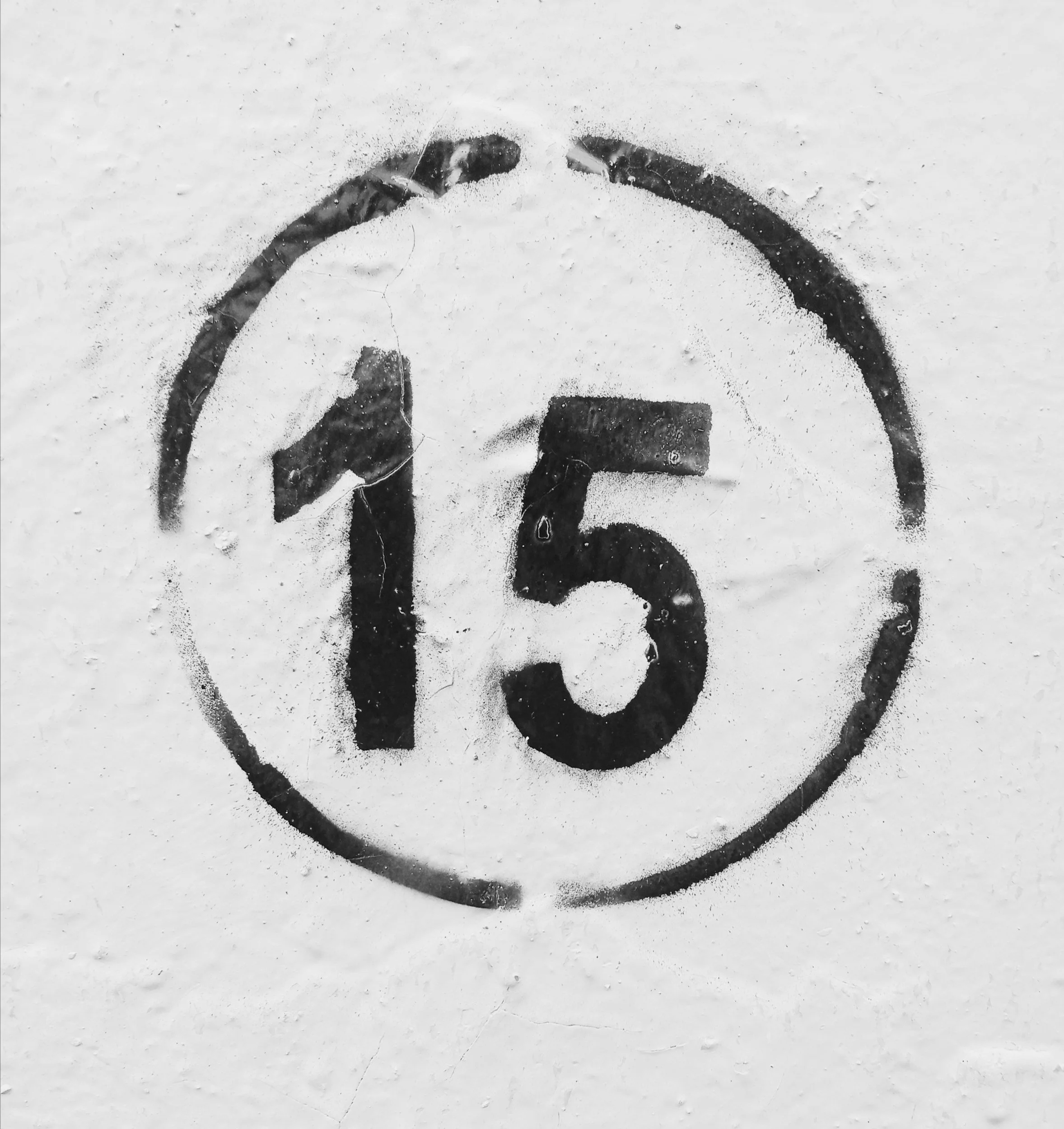 Black and white painted sign of the number 15 inside a circle on a white wall.