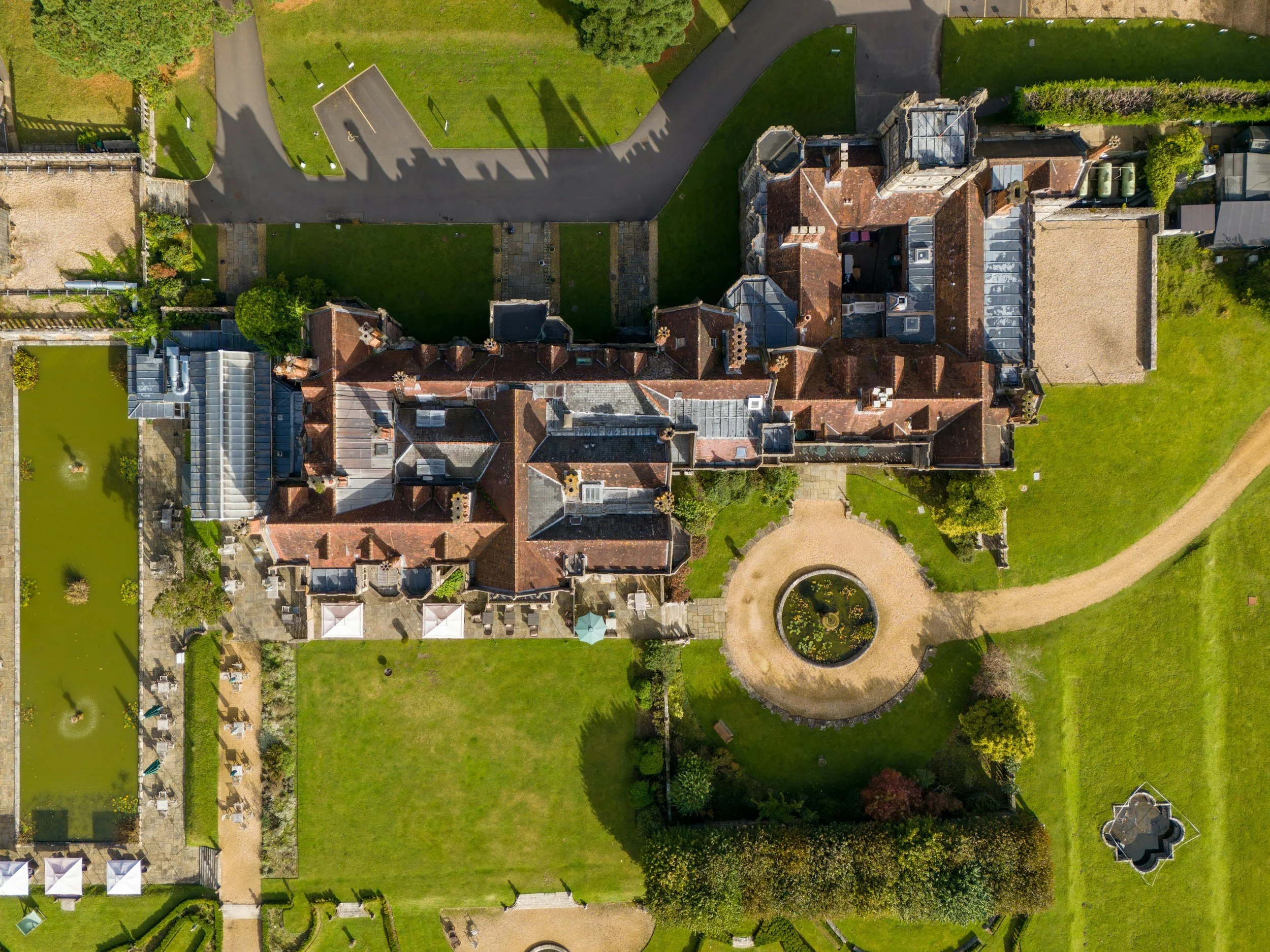 An aerial view of a large historic estate with a main building, gardens, pond, and surrounding grounds.