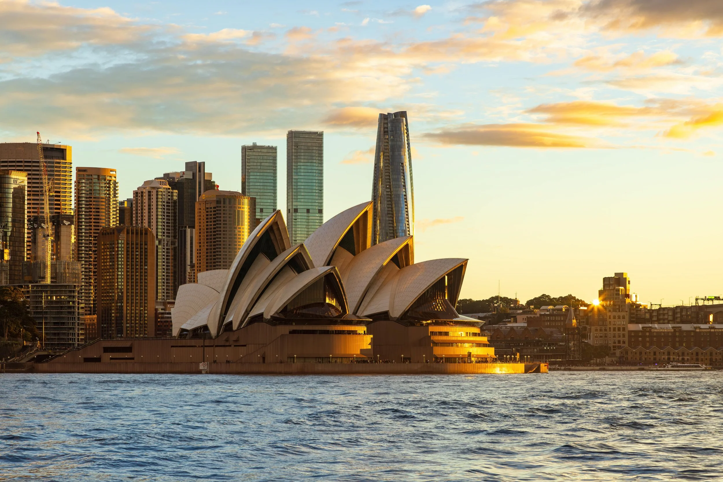 Sydney Opera House and city skyline during sunset with water in the foreground.