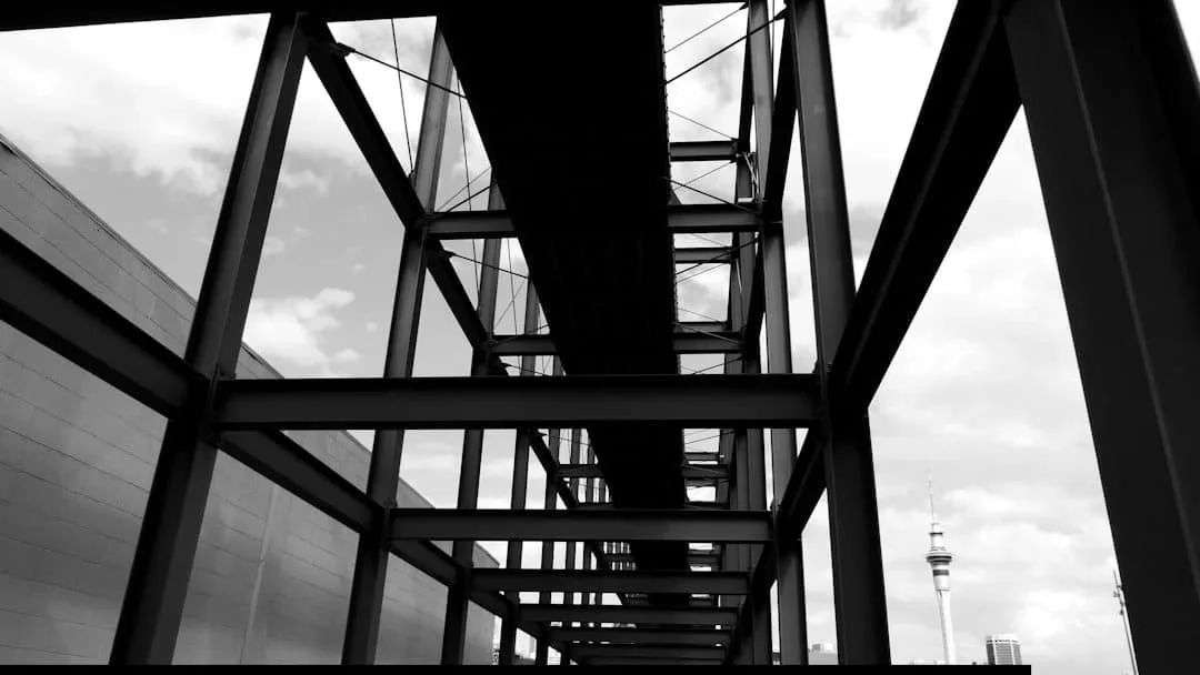 Steel beams and a suspended walkway frame the sky, with BCA city tower visible in the background under scattered clouds.