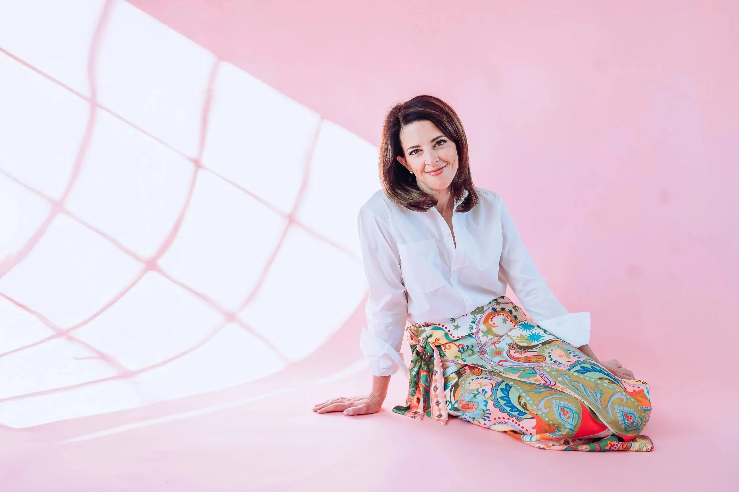 Relaxed and welcoming therapist seated on the floor against a pink backdrop, representing a calm, supportive, and nonjudgmental counseling presence.
