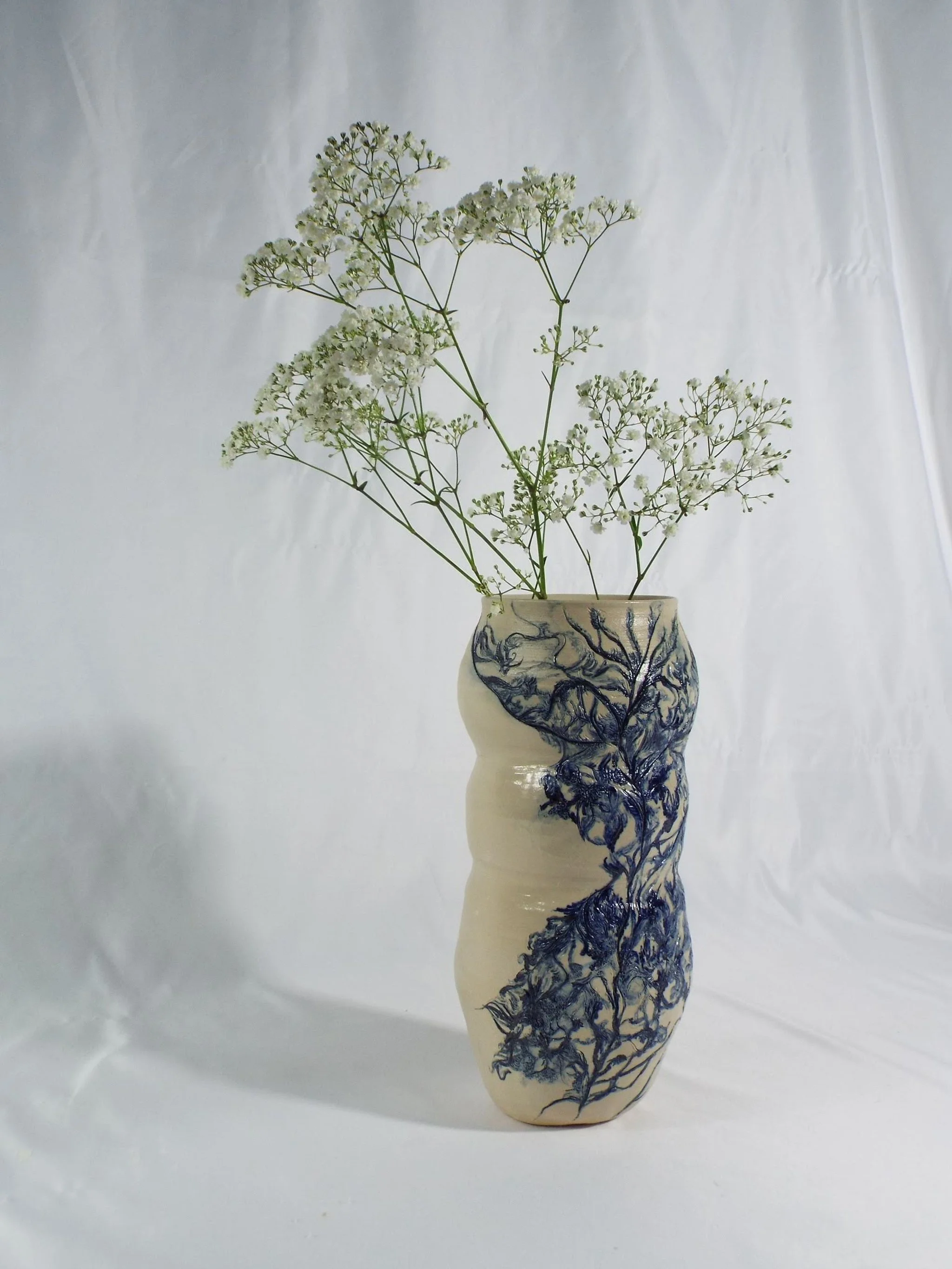 A white ceramic vase with blue painted floral designs, holding white delicate flowers, set against a light background.