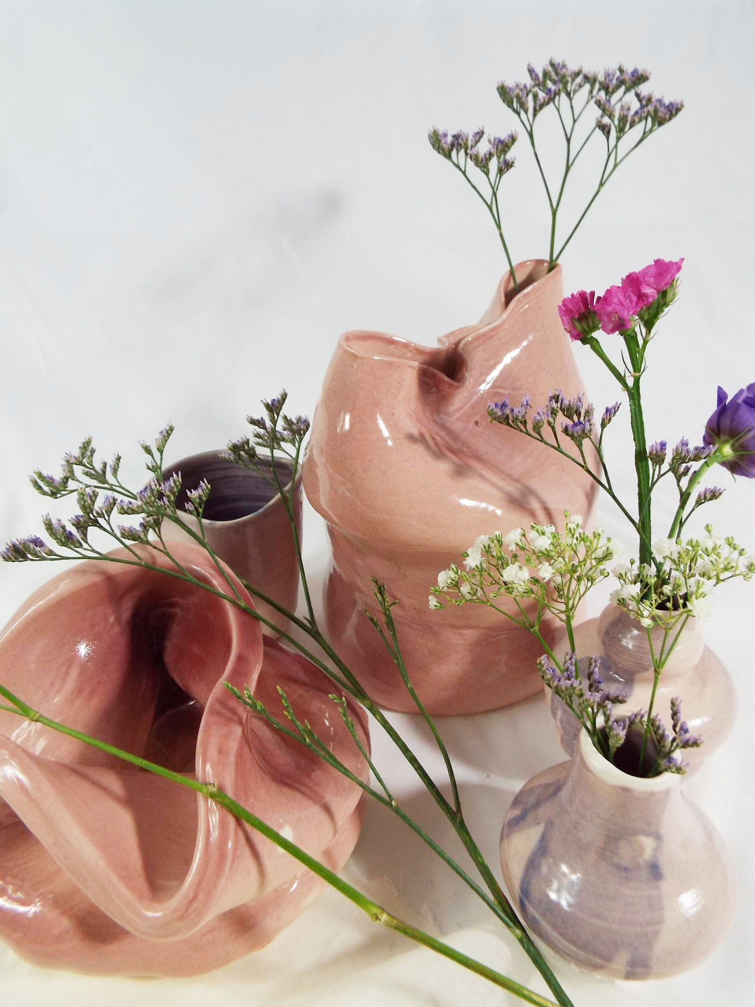 Multiple pink and purple ceramic vases with lavender and pink flowers arranged against a white background.