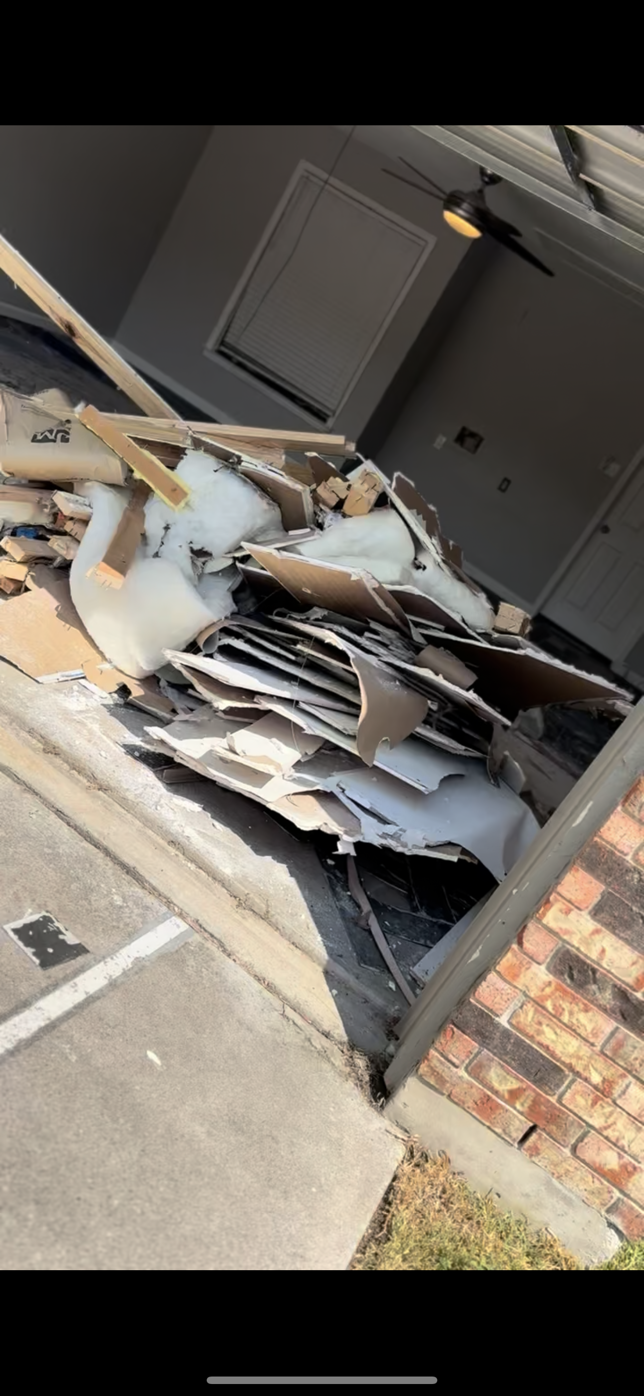 Pile of broken drywall, insulation, and debris in a garage or construction area outside a building.