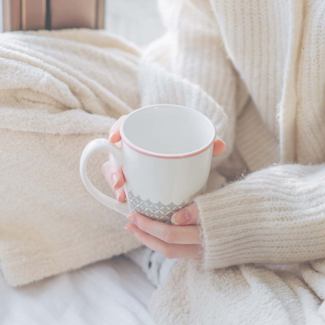 Hands holding a mug while seated indoors, suggesting a quiet, reflective moment.