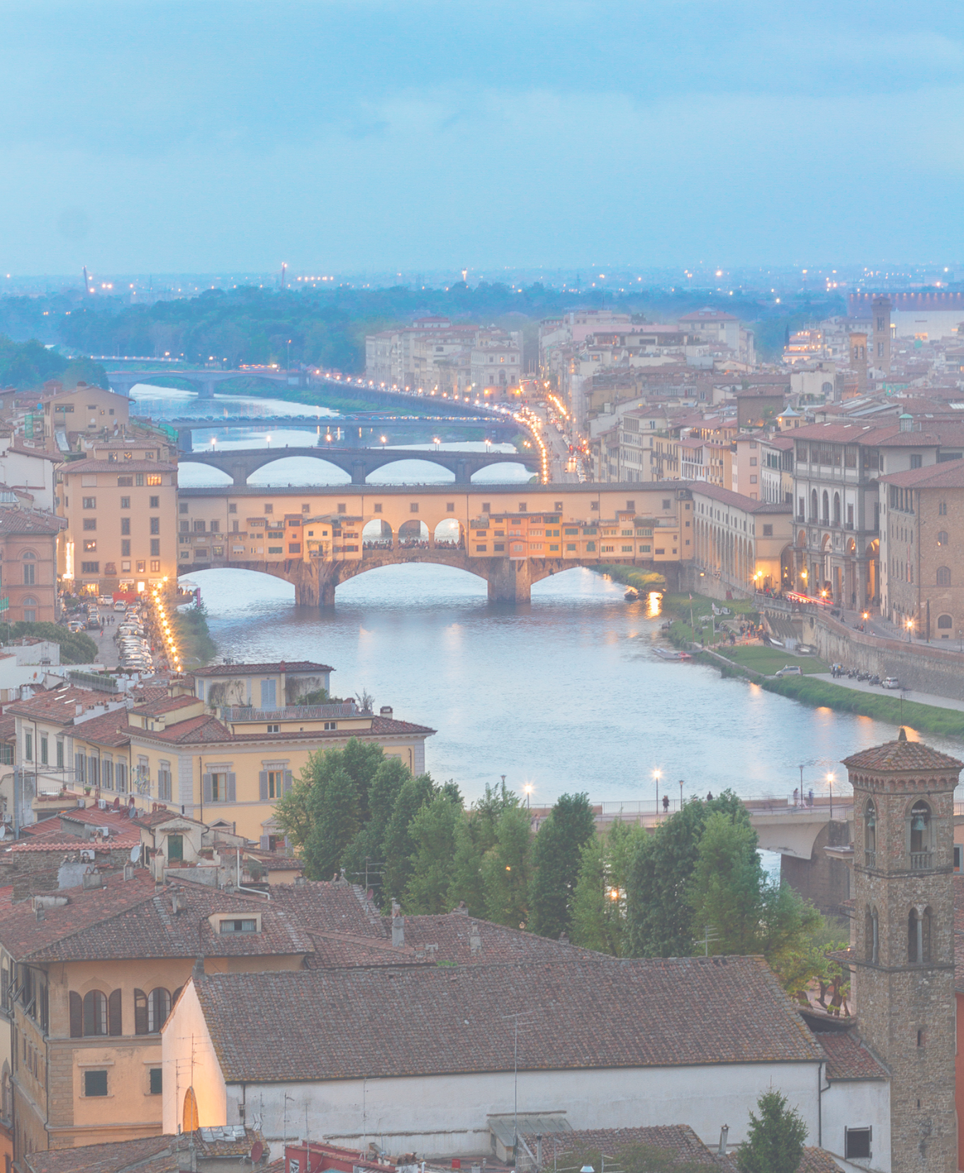 A quiet European cityscape with a river and bridges at dusk, viewed from above.