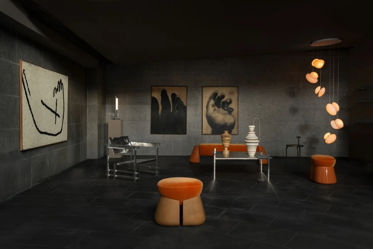 Salle d'exposition avec œuvres d'art modernes, y compris un tableau abstrait, deux peintures dans le fond, et un mobile suspendu avec des formes ovales. Décoration élégante avec des meubles en orange et en métal.