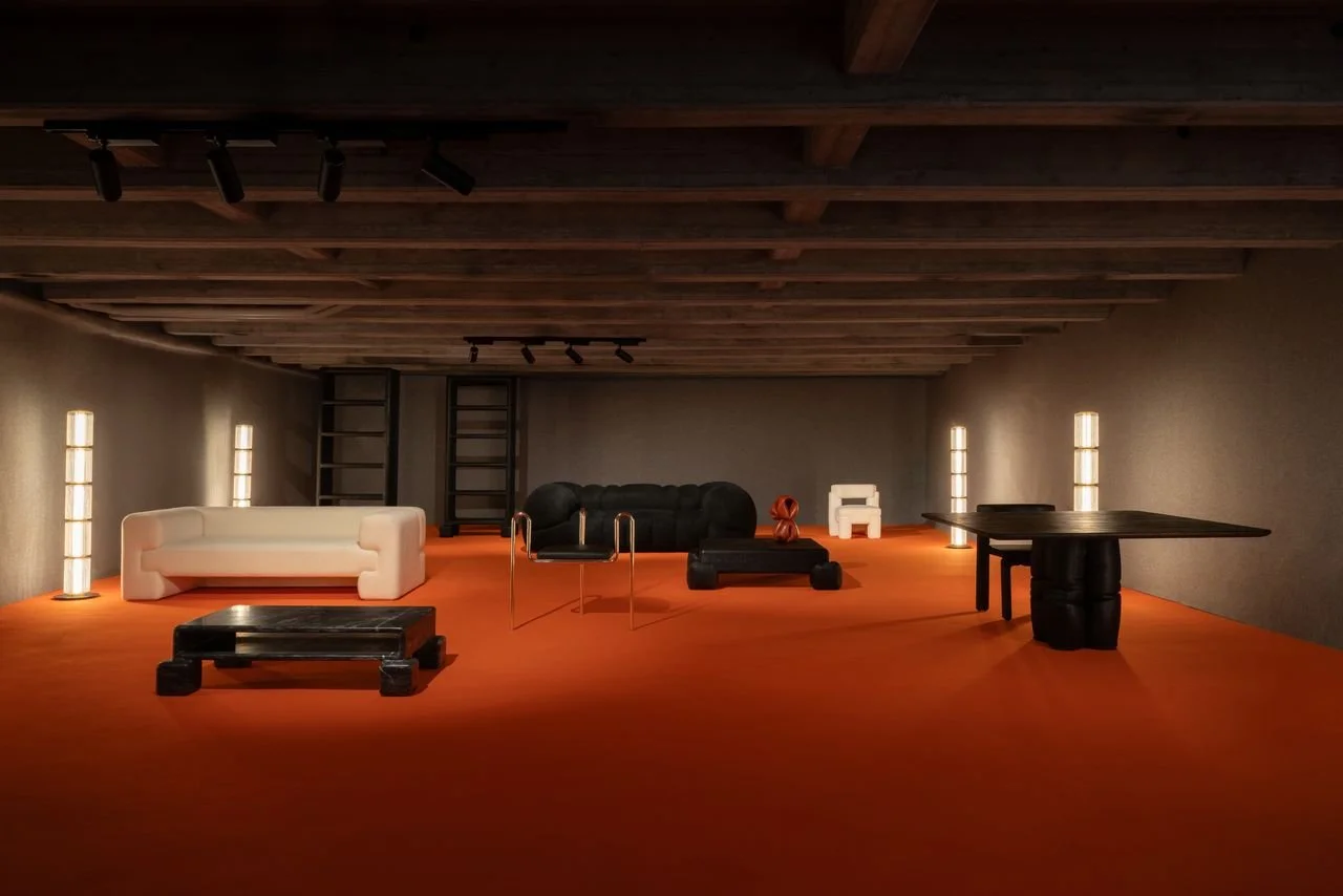 Salle d'exposition avec des meubles modernes, incluant un canapé blanc, un canapé noir, une table basse noire, une table rectangulaire et des deux petits tabourets blancs