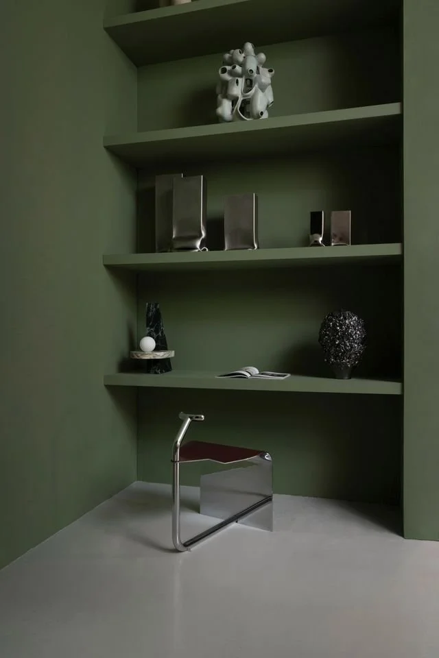 Une scene avec une étagère verte dans l'alcove d'un mur avec des objets décoratifs d'artisans contemporains avec fauteuil en métal