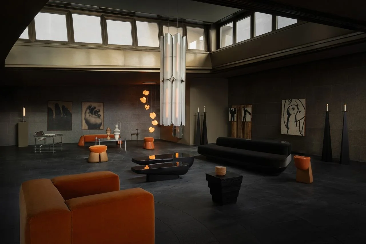 Salle de séjour moderne avec des meubles orange et noirs, un éclairage suspendu, des œuvres d'art abstraites sur le mur, et des bougies allumées.