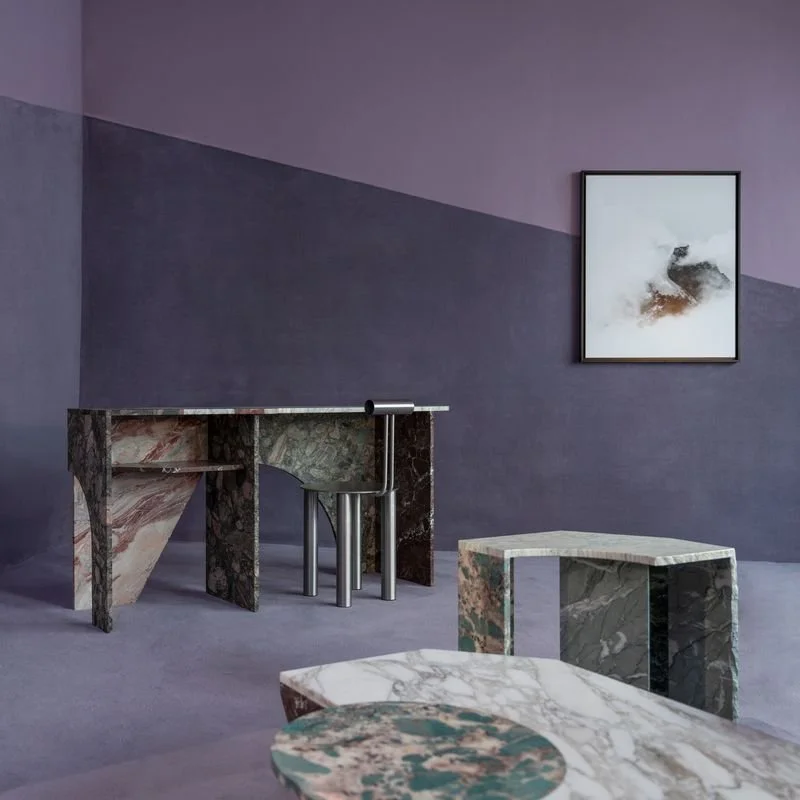 Une pièce moderne avec des meubles en marbre, un tableau abstrait sur un mur parme, et un mélange de meubles en marbre à motifs variés.