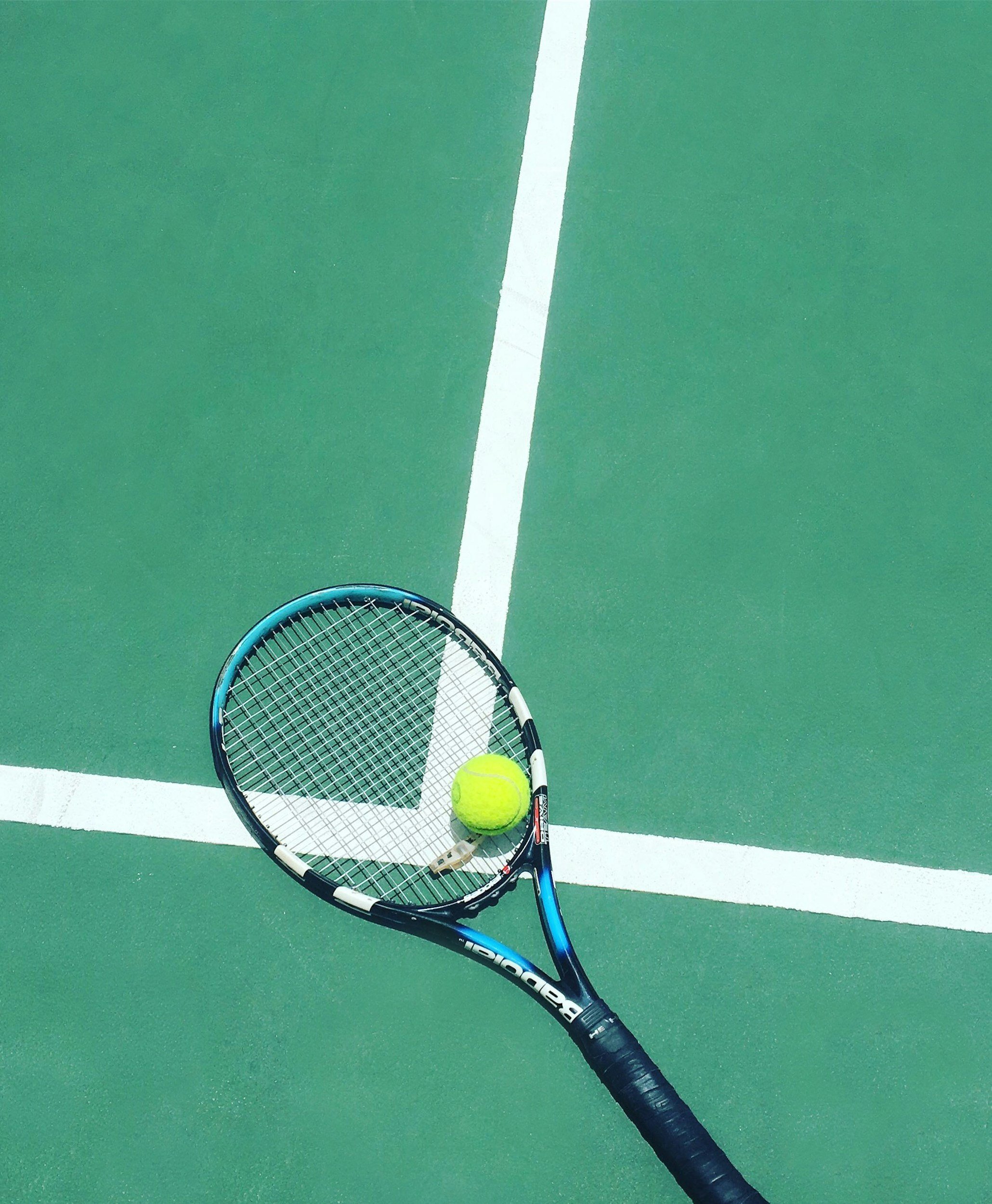 A tennis racket and a tennis ball on a green tennis court with white lines.