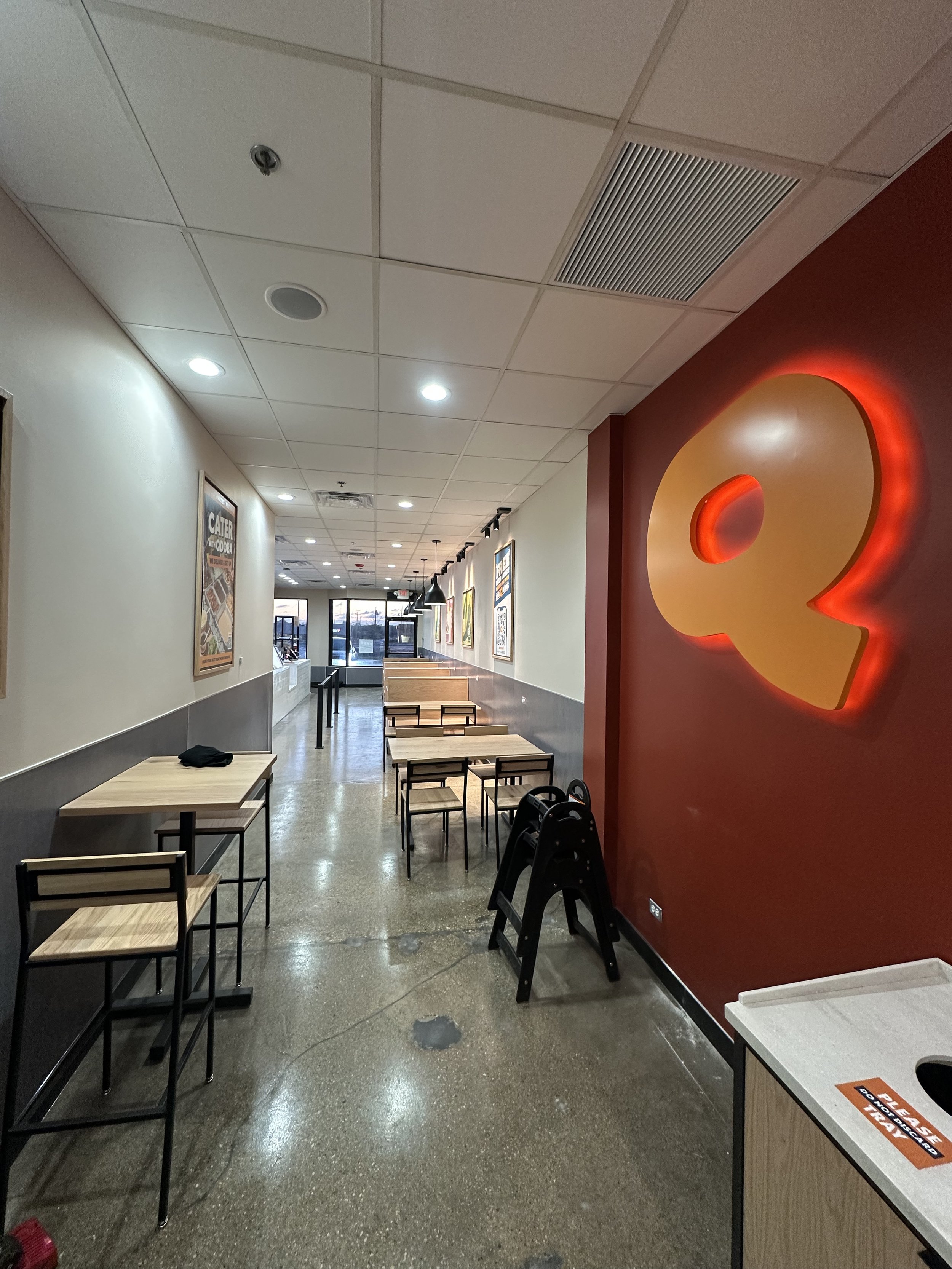 narrow eating area with small wooden tables and chairs, Q on red wall