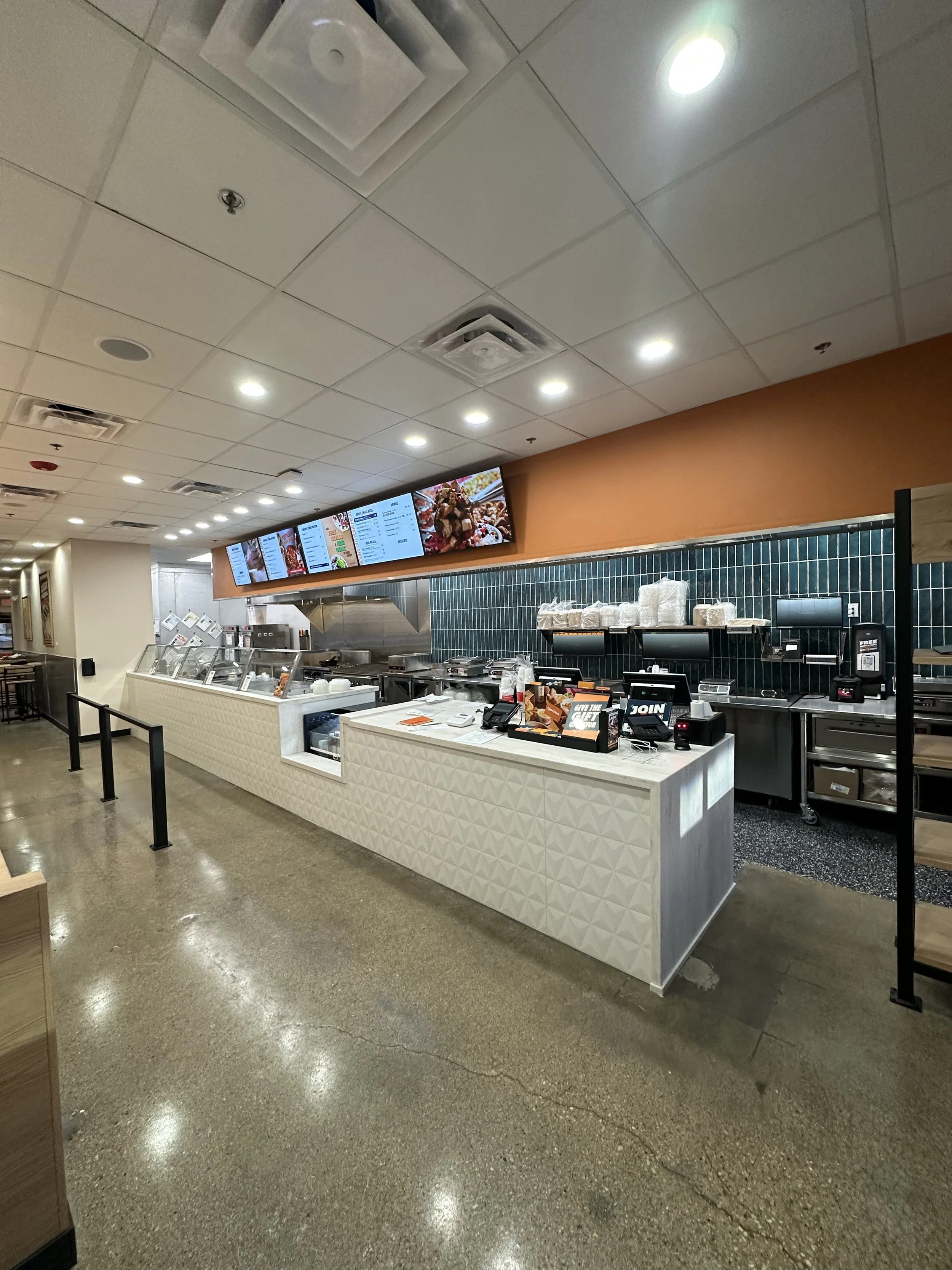 Qdoba restaurant counter with digital menus above, teal tile wall behind, cash register at the end