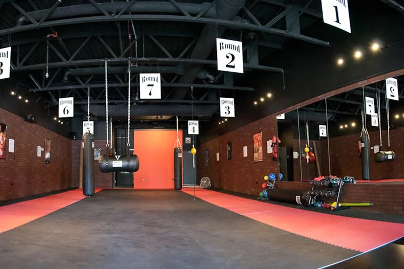 interior boxing gym, hanging bags in stations, red mats, weights