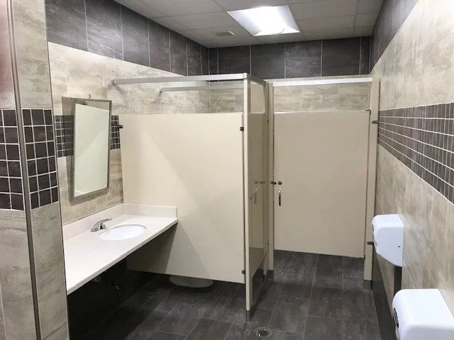 commercial bathroom stall, tile wall and mirror above sink