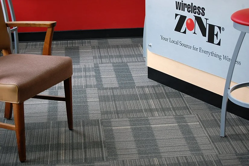 Verizon store interior, gray carpet next to wood desk with metal Wireless Zone sign and red and gray stool next to it