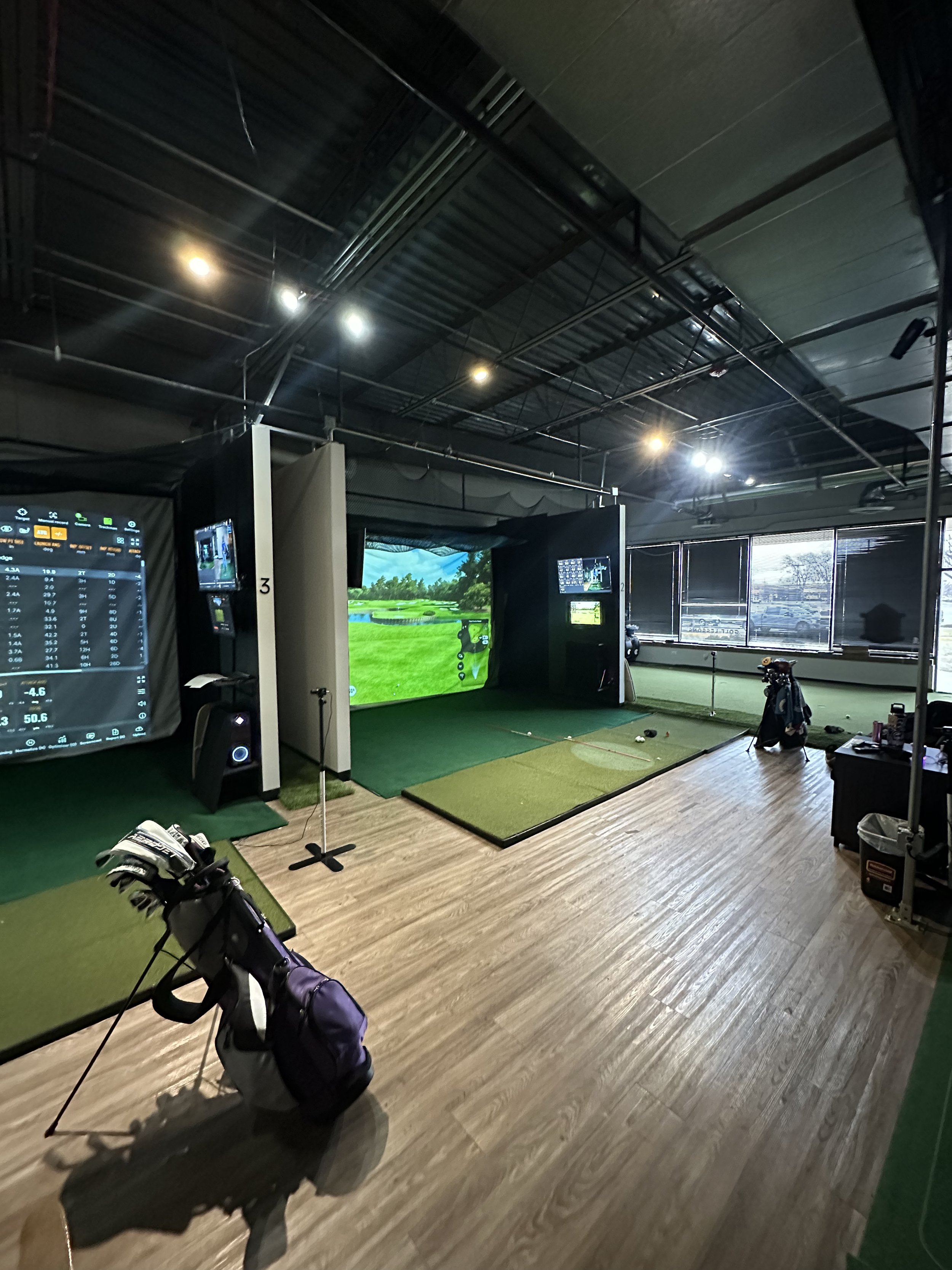 indoor golf simulator with wood floor and golf mats, large screens, high ceilings, and inviting lighting